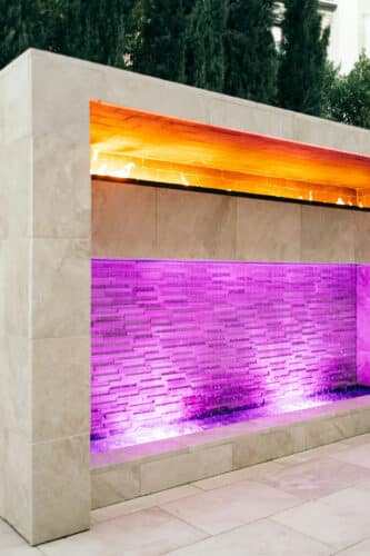 Purple lit waterfall with fireplace above
