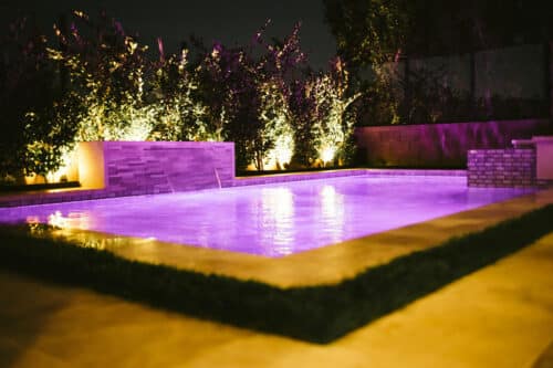 Lit purple lights in pool with waterfall