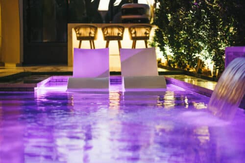 Purple lit pool with waterfall fountain and pool chairs