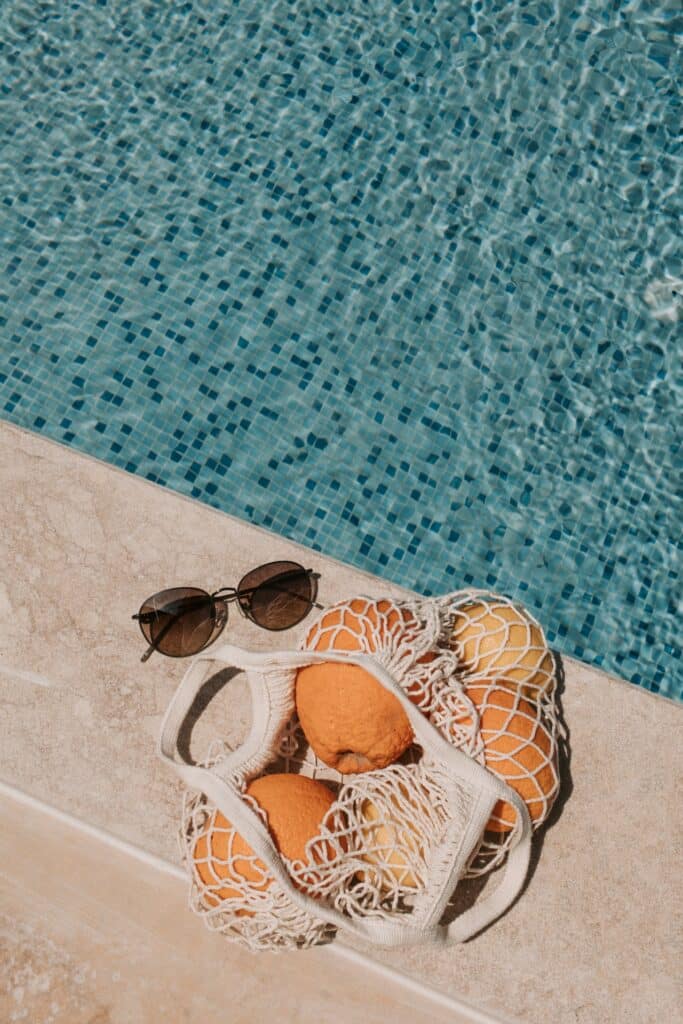 sunglasses and bag of oranges next to a remodeled pool in a backyard