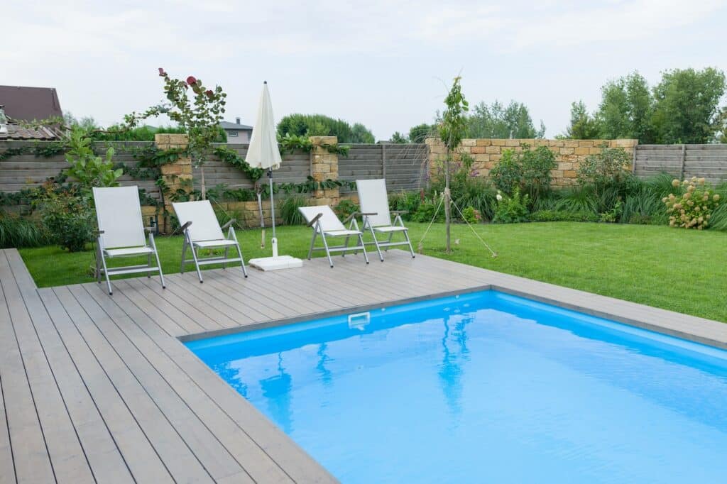 backyard inground pool surrounded by pool furniture and lawn