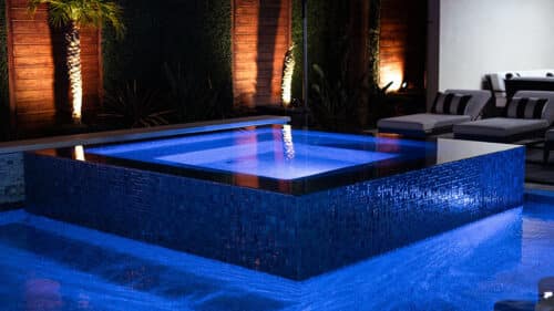 custom backyard pool with a hot tub at night