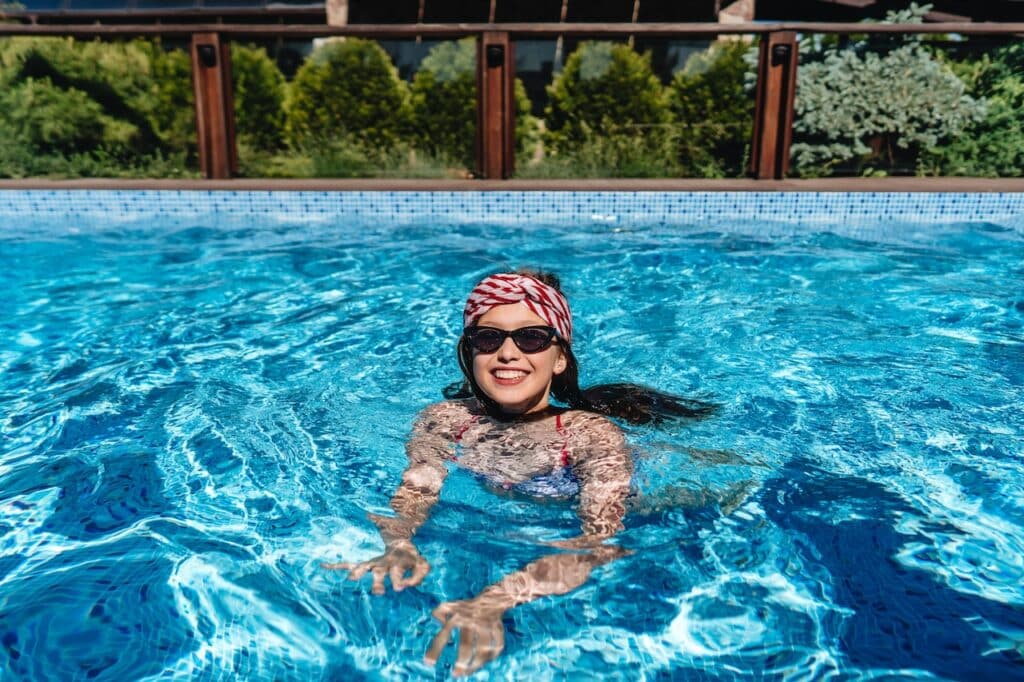 woman swimming in backyard swimming pool surrounded by trees and shrubs