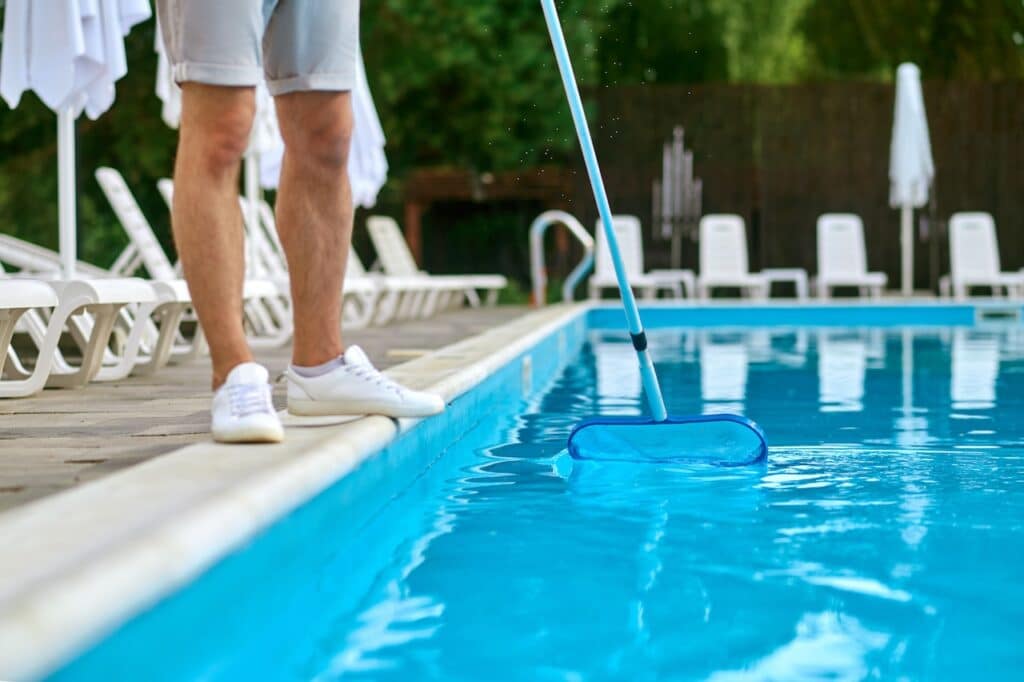 pool service person skimming backyard pool