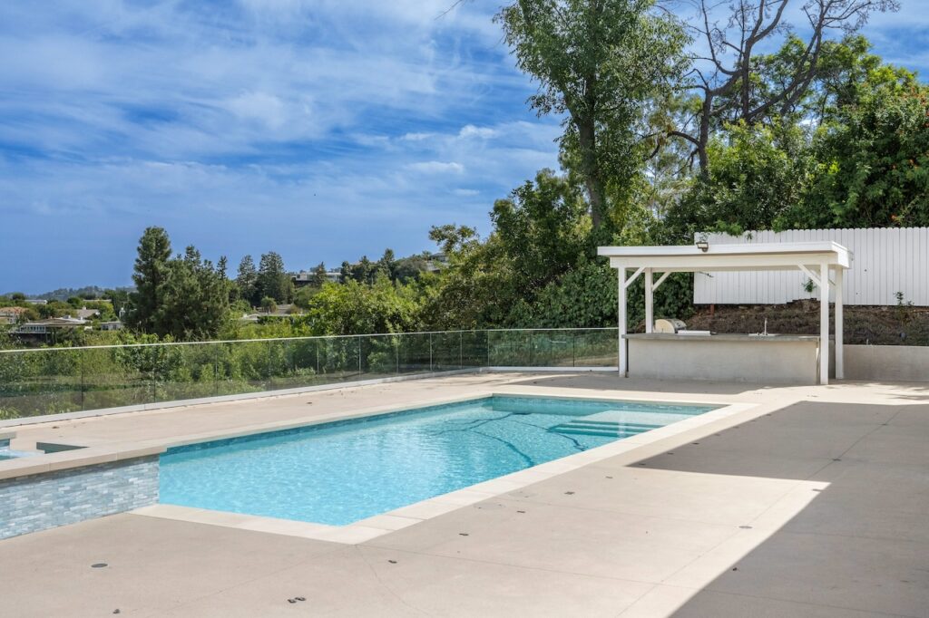 backyard swimming pool with pool deck and trees surrounding